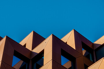 Obraz premium Geometric Form Architecture Shape Building Minimalist Abstract Urban Lines Exterior Featuring Sharp Angular Rooftops Symmetrical Patterns And Rhythmic Projections Under Clear Blue Sky