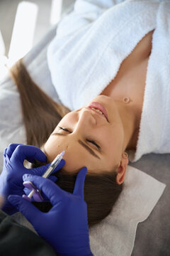 Smiling woman receiving injection in forehead zone at beauty clinic