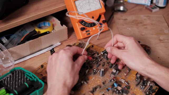 Close-up of an electronics technician using analog multimeter probes to test components on a circuit board. The vintage equipment contrasts with modern repair tasks and diagnostics.