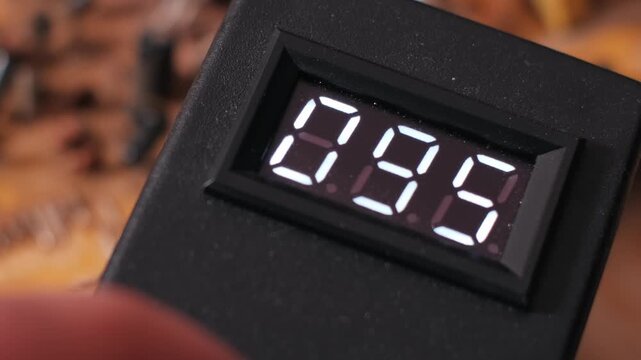 Close-up macro view of a digital voltmeter display showing rapidly fluctuating voltage readings. The unstable numbers suggest electrical circuit testing and diagnostic measurement.