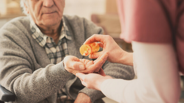 Hand of nurse giving pills to elderly male patient	