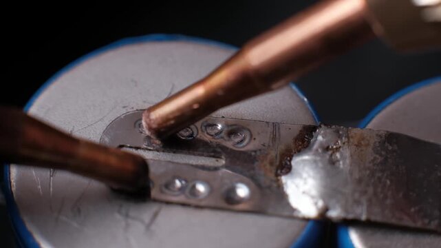 Macro slow motion shot of copper electrodes creating sequential weld points on a battery cell. Bright sparks highlight the heat and precision of the resistance welding process.