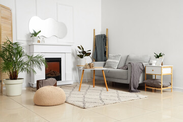 Obraz premium Interior of light living room with mirror, grey sofa and fireplace