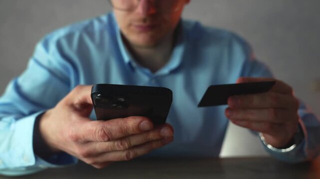 Focused young manager using a smartphone alongside a credit card to verify account balance and complete online transactions. Concept of digital payments and personal finance management.