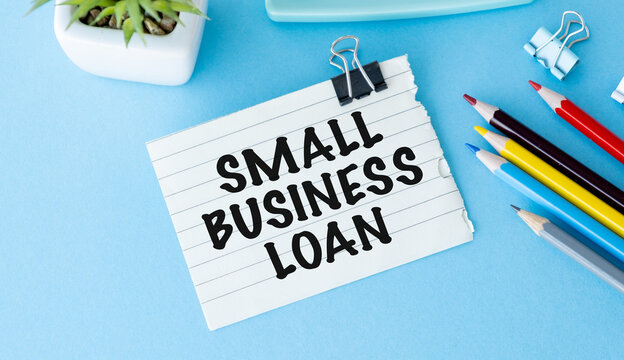 Small business loan written on lined paper. Clip holds note above blue desk surface.