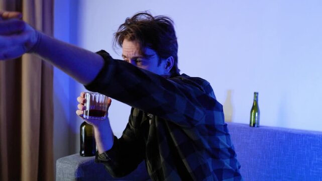 Aggressive drunk man pushes away a person holding an empty wallet. He drinks alcohol from a glass on the sofa. Concept of alcoholism, poverty, domestic violence, and financial crisis. 4k footage