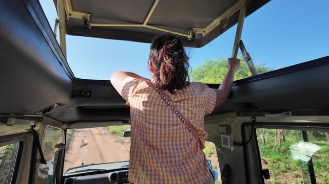 Frau steht in einem offenen Safari Gel&auml;ndewagen mit Hubdach w&auml;hrend der Fahrt