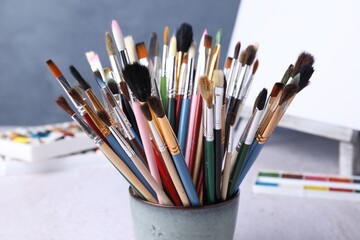Fototapeta premium Paintbrushes, paints and easel with canvas on table near blue wall, closeup
