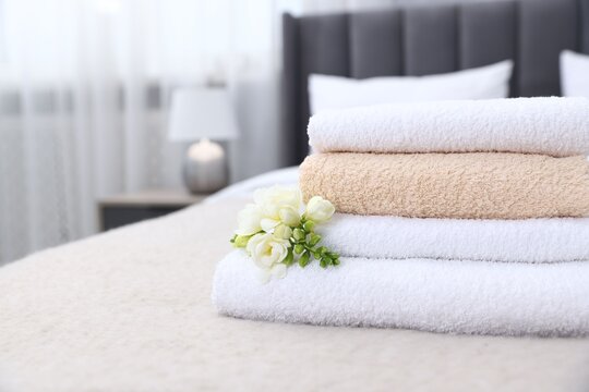 Fresh towels and beautiful freesia flowers on bed indoors, closeup. Space for text