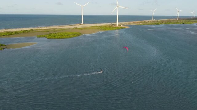 Kitesurfer rides shallow lagoon at Praia da Ta&iacute;ba S&atilde;o Gon&ccedil;alo do Amarante Cear&aacute; Brazil with onshore wind turbines along sand barrier and Atlantic coast, drone tracking shot