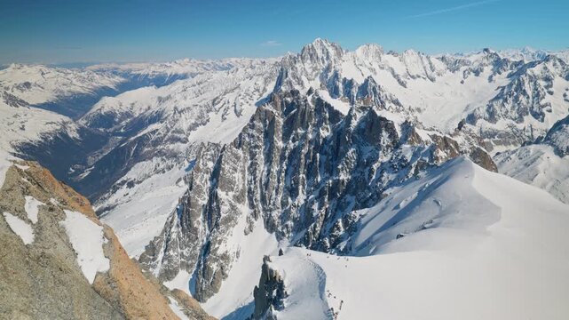 A sweeping high-altitude panorama from above Chamonix reveals dramatic jagged rocky peaks, deep glacial couloirs, and vast snowfields stretching across the French Alps under a clear winter sky.