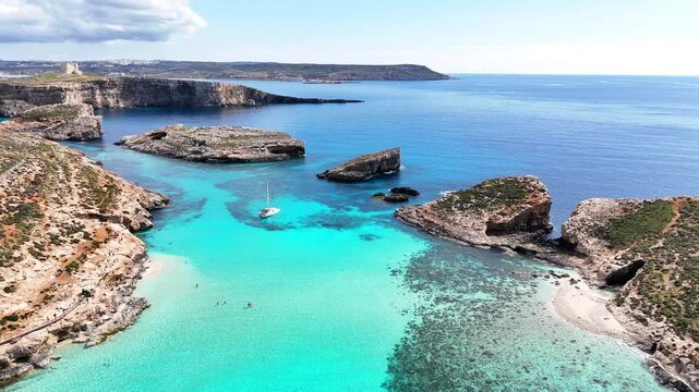 Blue Lagoon in Comino Għajnsielem Gozo Region Malta with shallow turquoise basin over limestone seabed and isolated islets in clear Mediterranean water with low human impact and no pollution, aerial