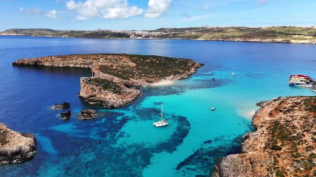 Aerial view of Blue Lagoon in Comino Malta with several boats anchored in clear turquoise water surrounded by rocky coastline and small island formations.