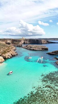 Blue Lagoon in Comino Għajnsielem Gozo Region Malta with shallow turquoise water over limestone seabed and small boats navigating between Comino and Cominotto islands, clear Mediterranean sea vertical