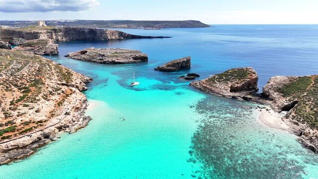 Aerial view of Blue Lagoon in Comino, Malta with a small boat anchored in clear turquoise water, surrounded by rocky islets, sandy seabed, and coastal cliffs.
