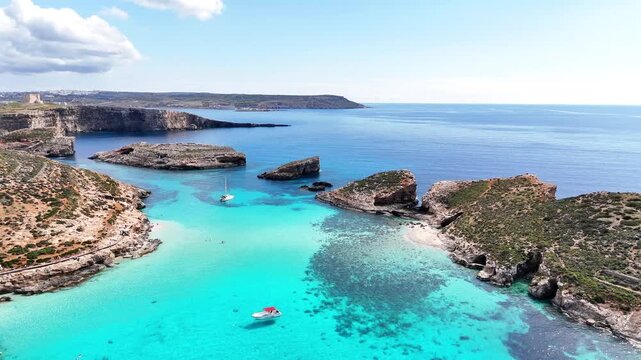 Blue Lagoon in Comino Għajnsielem Gozo Malta with shallow turquoise water over limestone seabed and small islets between Comino and Cominotto, clear Mediterranean sea and coastal morphology, aerial