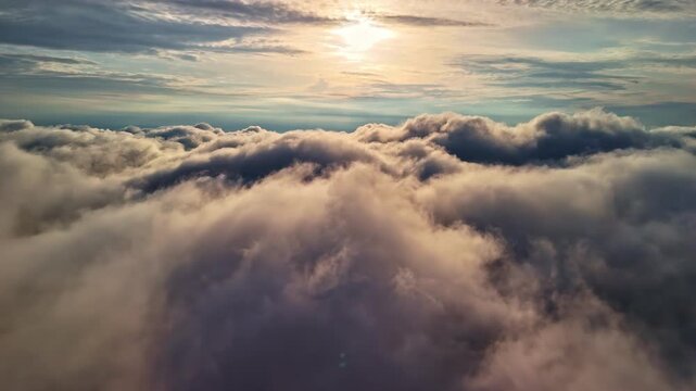 Aerial Dolly Out Above Fluffy White Clouds Toward Golden Sun in Bright Blue Sky