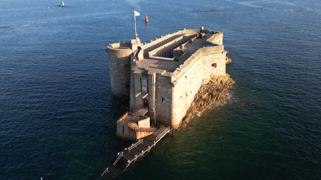 Aerial view of Chateau du Taureau, a stone fortress standing defiantly against the crashing waves, its flag fluttering in the breeze, Plouezoc'h, Bretagne, France.
