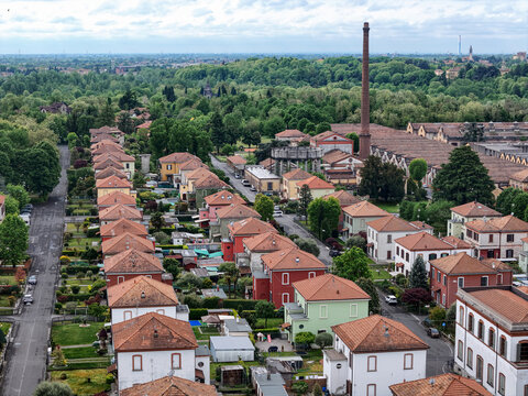 Aerial view of Industrial Village of Crespi d'Adda with its characteristic rows of workers' houses, red-tiled roofs, and the iconic tall brick chimney in Capriate San Gervasio, Lombardia, Italy.