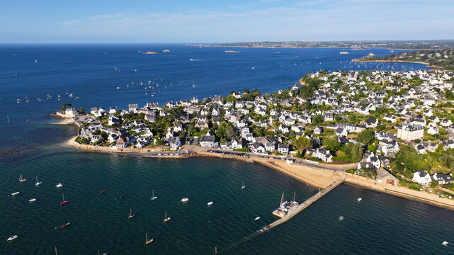 Aerial view of a quaint coastal town with boats dotting the shimmering water and a long pier stretching into the sea, Carantec, France.
