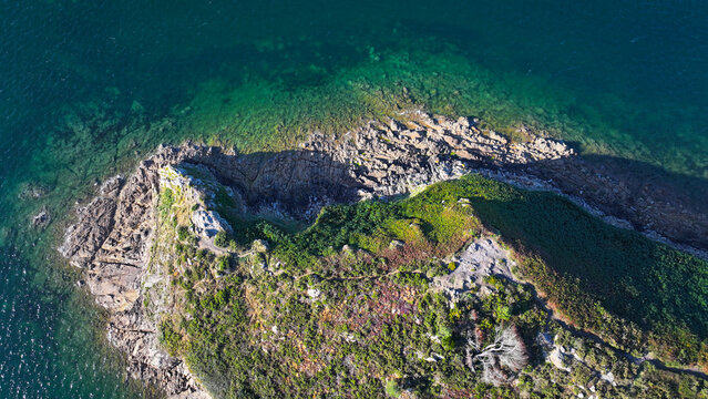 Aerial view of a rugged, verdant headland reaching into the shimmering emerald and sapphire waters, Carantec, Bretagne, France.