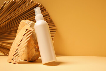 Naklejka premium Stone with hair spray, comb and palm leaf on yellow background
