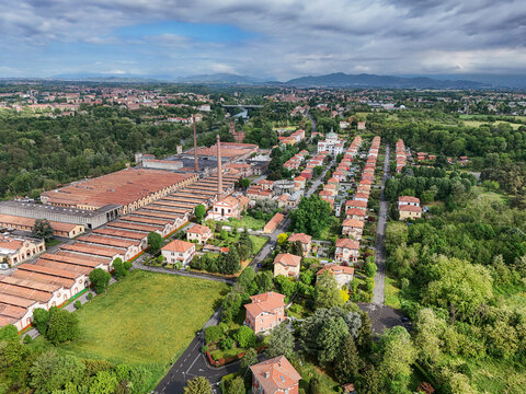Aerial view of the Industrial Village of Crespi d'Adda with its historic factory buildings, tall chimneys, and worker houses surrounded by greenery in Capriate San Gervasio, Lombardia, Italy.