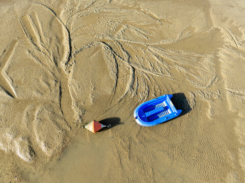 Aerial view of a small blue plastic boat and an orange marker resting on the rippled, sandy shores of Bourcefranc-le-Chapus, Bourcefranc-le-Chapus, France.