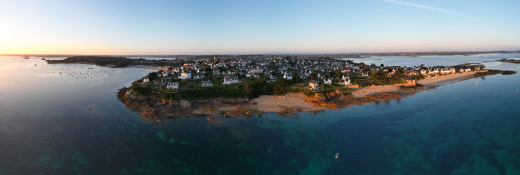 Aerial view of the serene Plage du Kelenn, where golden sands meet the translucent turquoise waters, framed by white houses under a soft morning glow, Carantec, Bretagne, France.