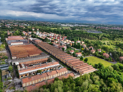 Aerial view of the Industrial Village of Crespi d'Adda with its historic factory buildings and tall chimneys surrounded by green trees in Capriate San Gervasio, Lombardia, Italy.