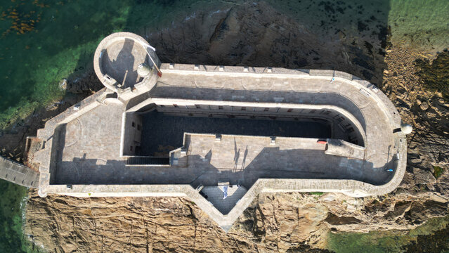 Aerial view of the ancient Chateau du Taureau, a formidable stone fortress rising from rugged brown rocks amidst sparkling turquoise waters, Plouezoc'h, Bretagne, France.