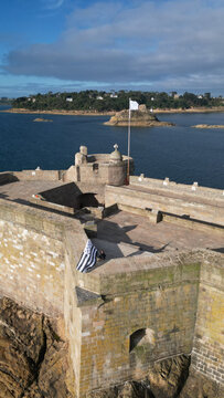 Aerial view of the historic Chateau du Taureau, a weathered stone fortress on its rocky island, stark against the deep blue sea, Plouezoc'h, Bretagne, France.