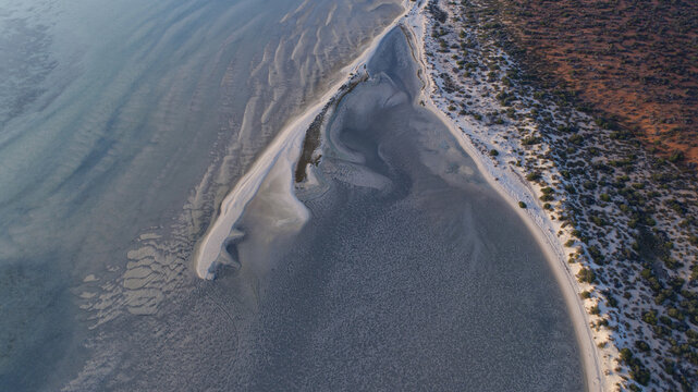 Aerial view of a white sandbar dividing shallow blue waters from the rugged reddish coastline, Denham, Western Australia, Australia.