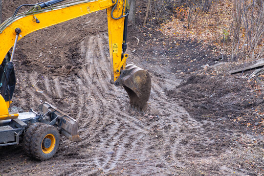 Yellow backhoe loader working on dirt construction site with tire tracks on wet ground.