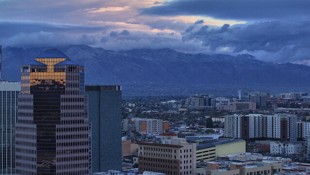 Aerial view of skyscrapers piercing the twilight sky as the Santa Catalina Mountains loom in the distance, their peaks veiled in ethereal clouds, Tucson, Arizona, United States.