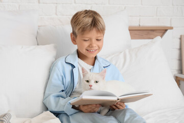 Naklejka premium Cute little boy with cat reading book in bedroom