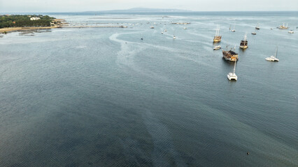 Aerial view of traditional phinisi boats and catamarans anchored in a calm tropical bay with a pier and distant island © Made