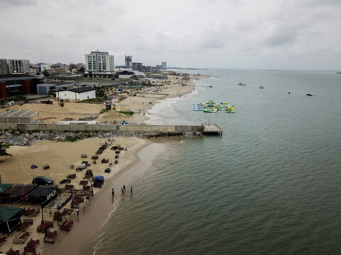 Aerial view of vibrant inflatable water park on ocean, by sandy beach, concrete pier, and coastal city, Lagos, Lagos, Nigeria.
