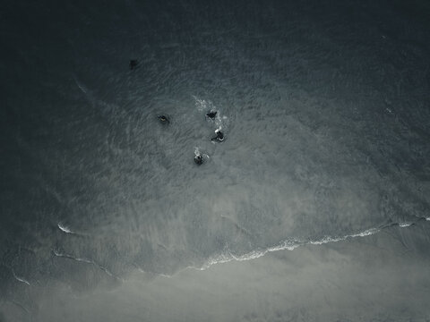 Aerial view of dark, brooding ocean waters churning around mysterious rocky outcrops, with a gentle white foamy surf kissing the shore, Lagos, Lagos, Nigeria.