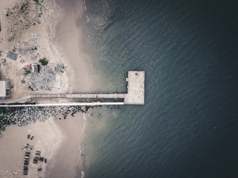 Aerial view of a robust concrete pier dramatically extending into the deep blue-green ocean from a rugged, sandy coastline, Lagos, Lagos, Nigeria.