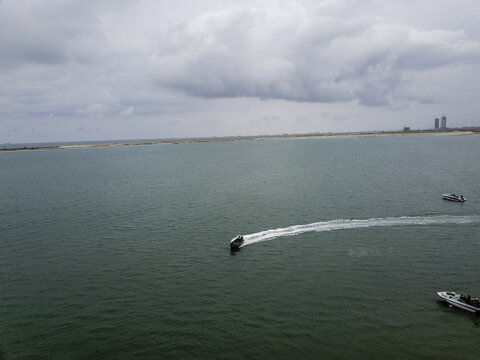 Aerial view of a boat's bright white wake across deep, dark water towards distant twin towers under a cloudy sky, Lagos, Lagos, Nigeria.