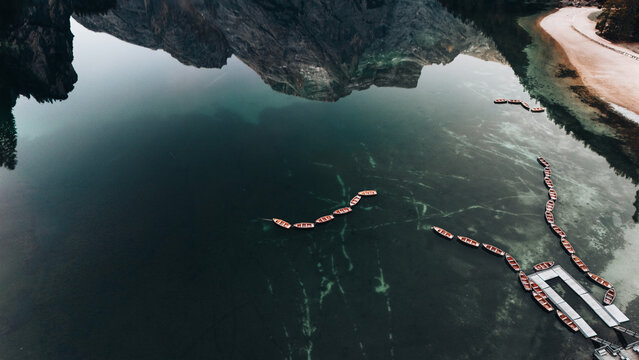 Aerial view of serene emerald waters reflecting the majestic, rugged peaks, with a chain of small wooden boats floating gently, Lago di Braies, Trentino-South Tyrol, Italy.