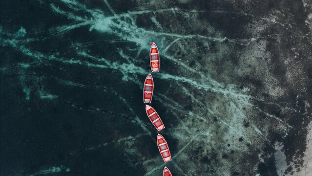 Aerial view of vibrant red boats gracefully aligned on the shimmering, patterned turquoise and dark waters of Lago di Braies, Lago di Braies, Trentino-South Tyrol, Italy.