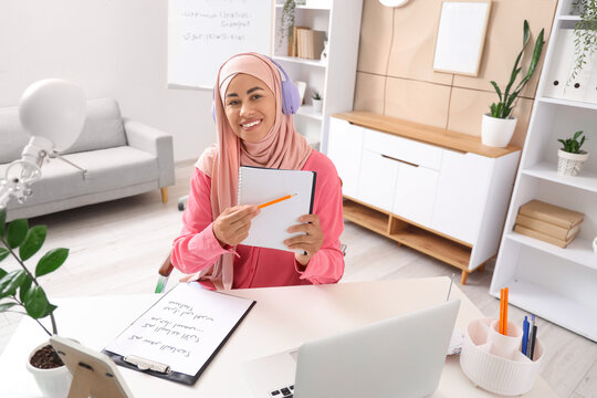 Young Muslim woman in headphones learning Arabic language online at office