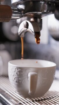 Espresso flowing from a portafilter into a white cup on a coffee machine. Cafe coffee preparation