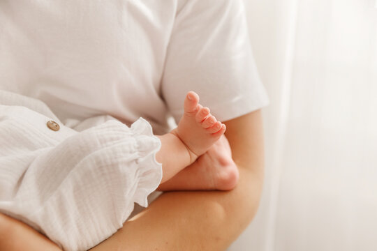 Close-up of tiny newborn baby feet held by mother, tender skin and white cotton clothes.