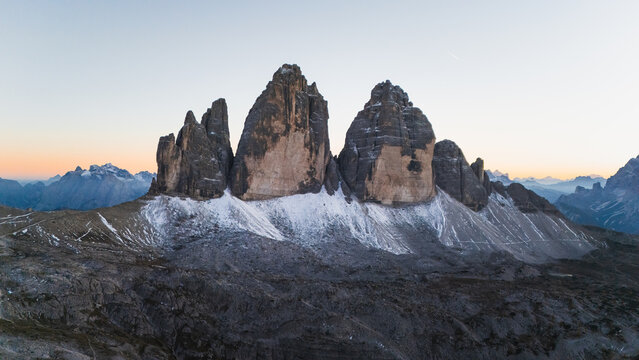Aerial view of Tre Cime di Lavaredo peaks, their dark rock and white snow contrasting against the soft, gradient sky, Tre Cime di Lavaredo, Veneto, Italy.