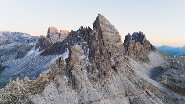 Aerial view of Tre Cime di Lavaredo's imposing grey peaks, their rugged textures defined against the soft, pale sky, Tre Cime di Lavaredo, Veneto, Italy.