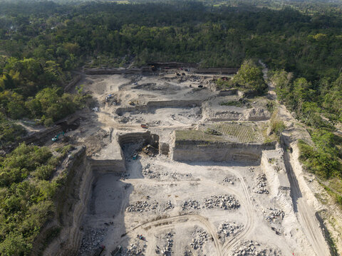 Aerial view of a vast open-pit mining operation, where raw earth is dramatically carved out amidst lush green forest, Klaten, Central Java, Indonesia.