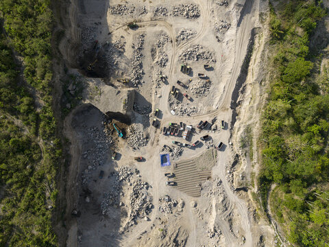 Aerial view of the quarry's raw textures and geometric patterns contrasting with the lush greenery, a stark juxtaposition of industry and nature, Klaten, Central Java, Indonesia.
